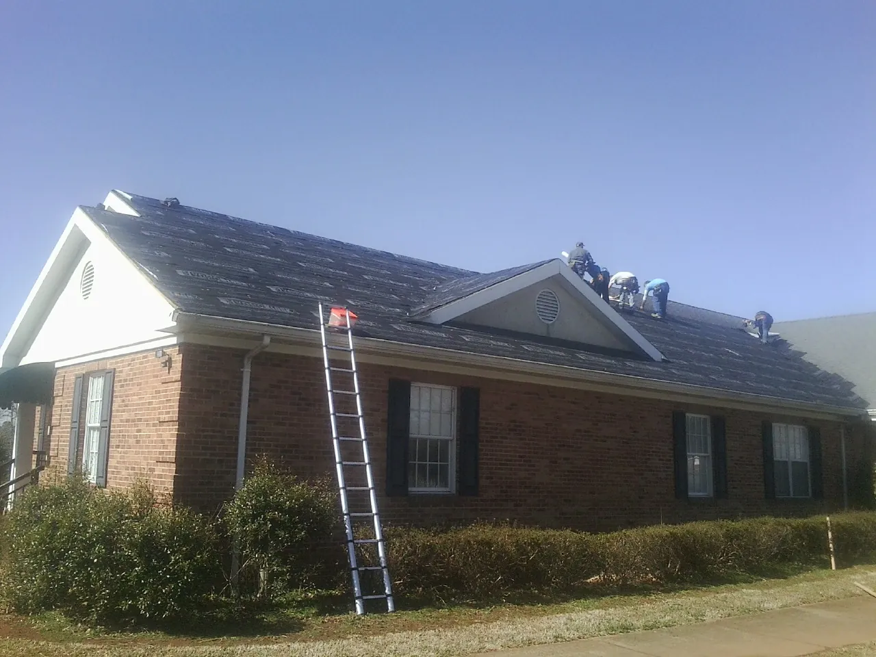 Crew tearing shingles off a brick ranch roof with a ladder set — Emergency Roof Repair work by our crew in Drumore
