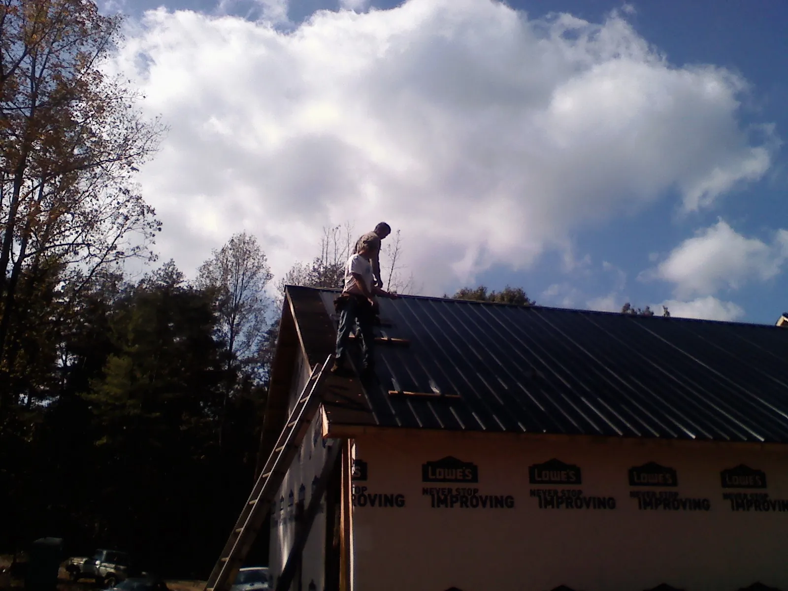 Roofer fastening dark metal panels high against a cloudy sky, from a Roof Inspection job in Drumore