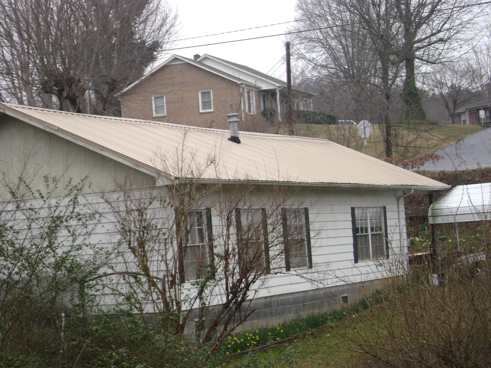 Tan metal roof on a white sided house set into a hillside — Commercial Roofing by Roofing Brothers in Drumore